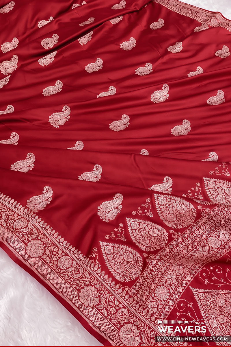 A pure red Banarasi silk saree with intricate silver zari paisley and floral motifs, featuring a wide decorative border, laid out on a white surface.
