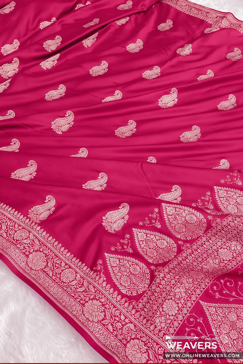 A close-up of a rich hot pink Banarasi silk saree with intricate gold zari paisley and floral motifs, featuring a wide decorative border.