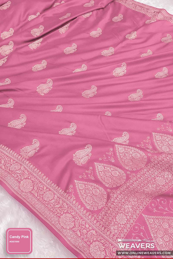 A pink Banarasi saree with intricate light pink and white paisley and floral motifs, featuring a wide decorative border, shown draped on a white surface.