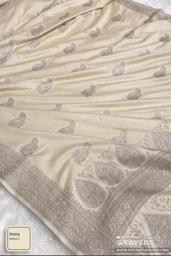 An ivory Banarasi silk saree with zari paisley and floral motifs, featuring a detailed border, 'Online Weavers' brandng, shown with a color swatch label in the bottom left corner.