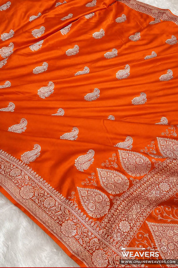 Bright orange mashru Banarasi silk saree with intricate silver paisley and floral zari motifs, featuring a wide decorative border and a small 'Online Weavers' watermark at the bottom right.