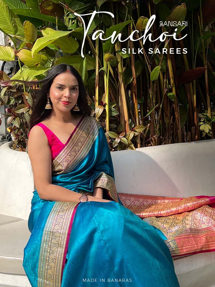 Woman in a tanchoi blue saree sitting on a bench with 'Banarasi Saree manufacturer' branding.