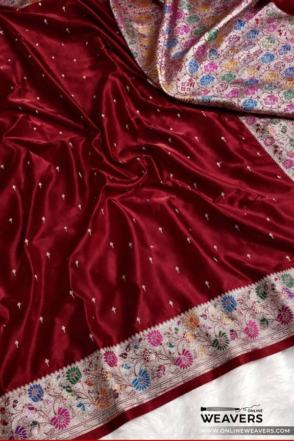 A close-up of a rich maroon red mashru silk saree, likely a Banarasi saree, featuring delicate silver zari embroidery, a colorful floral border, and a matching patterned inner lining-KL112
