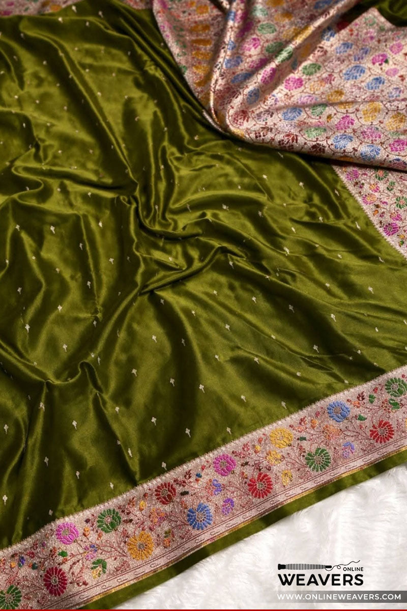 A close-up of a rich henna olive green mashru silk saree, likely a Banarasi saree, featuring delicate silver zari embroidery, a colorful floral border, and a matching patterned inner lining-KL114