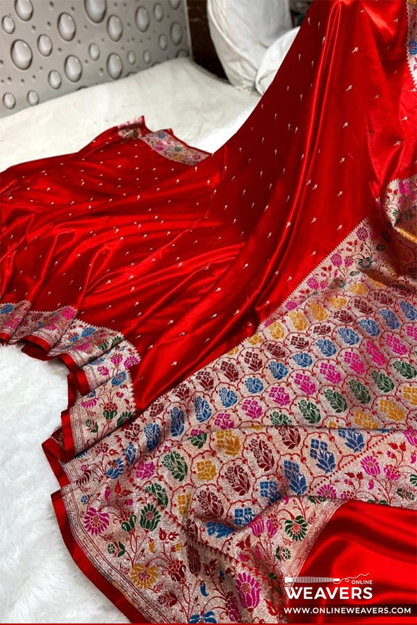 A red Banarasi silk saree in mashru silk with a heavily multicolor floral border displayed on a white bed. 'OnlineWeavers' branding