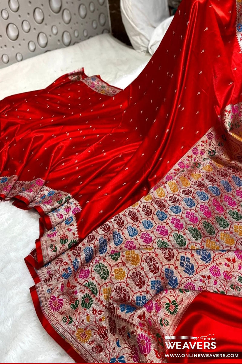 A red Banarasi silk saree in mashru silk with a heavily multicolor floral border displayed on a white bed. 'OnlineWeavers' branding